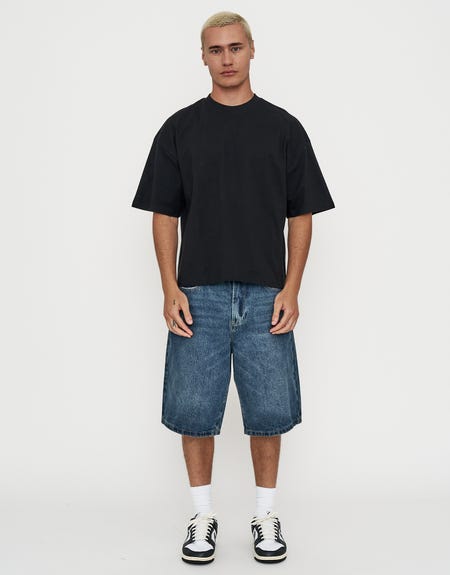 Black oversized tee with knee-length blue denim jorts, white crew socks and black-and-white sneakers